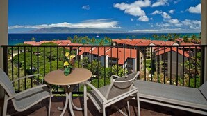 A balcony with a view of a coastal area, a table with chairs, and a vase with flowers.
