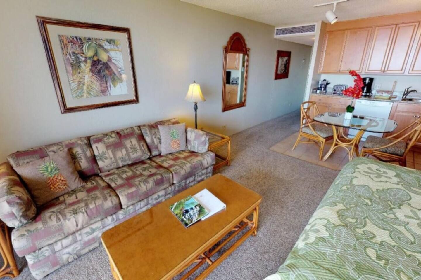 A living room with a sofa, coffee table, and a bed. There is a kitchen area with a dining table and chairs.