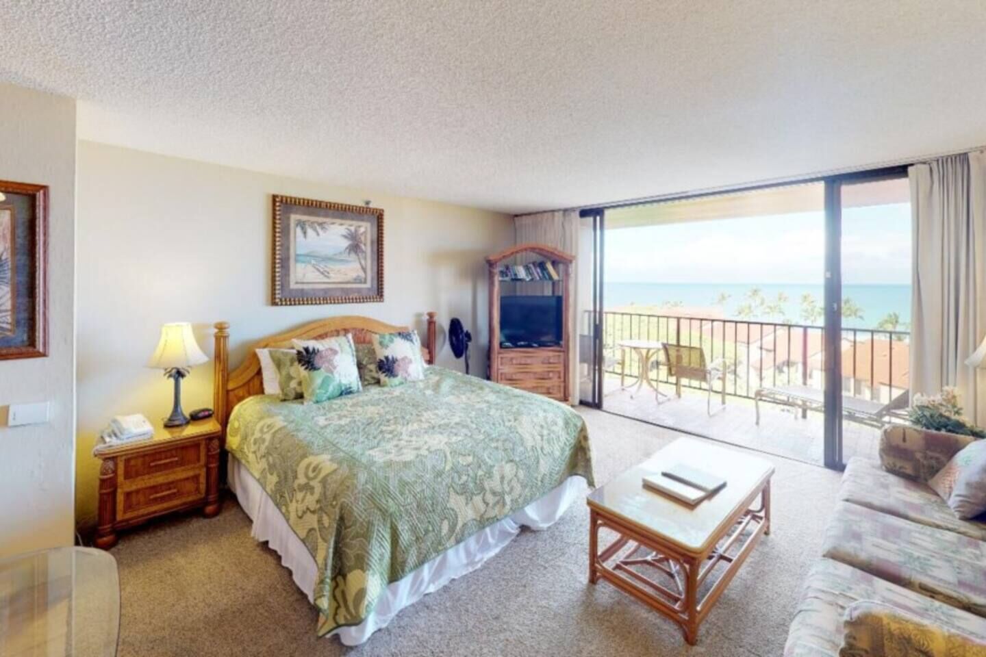 A hotel room with a bed, bedside table, lamp, and a view of the beach through a balcony.