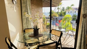 A glass-top dining table with wicker chairs, a potted orchid, and a view of a street with palm trees and houses. - Maui Special!! 2BDRM/2BA Ocean View and Convenient Location (Kihei)