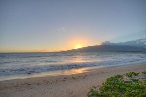 A beach with waves, a sunset, and a distant mountain.