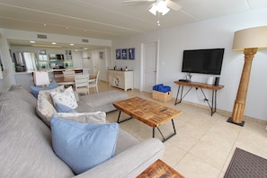 A living room with a sofa, coffee table, TV, and a kitchen in the background.