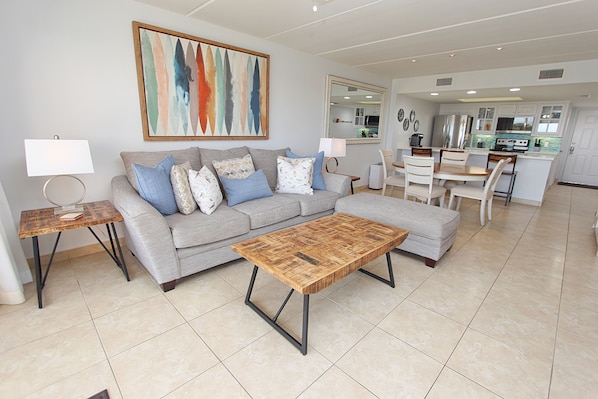 A modern living room with a grey sofa, a wooden coffee table, and a dining area with a white table and chairs.