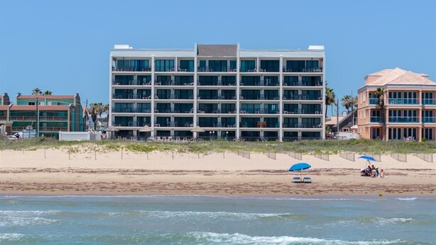 Un hotel amb diversos pisos i balcons, situat a la platja, amb una riba sorrenca i vista a l'oceà.