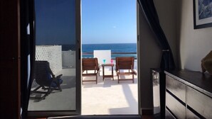 A room with a sliding glass door leading to a balcony with a view of the ocean.
