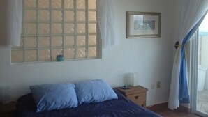 A bedroom with a bed, a nightstand, a window with curtains, and a framed picture on the wall.