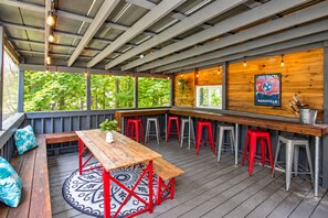 An outdoor patio area with a wooden table and red stools, a bar counter, and a poster on the wall. - Misty Court Hideaway Cozy + Private Retreat (Nashville)