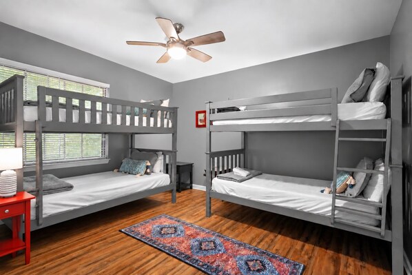 A room with two bunk beds, a ceiling fan, a window with blinds, a red nightstand, and a patterned rug. - Misty Court Hideaway Cozy + Private Retreat (Nashville)