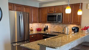 Una cocina moderna con encimeras de granito, electrodomésticos de acero inoxidable, armarios de madera y taburetes de bar.