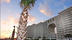 Un hotel de varios pisos con una entrada arqueada destacada y una palmera en primer plano.