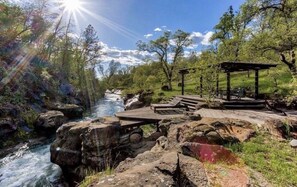 Ein Park am Flussufer mit einer Holzterrasse, Bänken und einem Gazebo.