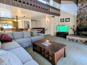 Ein Wohnzimmer mit einem Ecksofa, einem Holztisch, einem Fernseher und einem Kamin aus Stein.