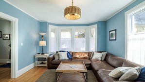 Ein Wohnzimmer mit braunem Ledersofa, einem Holztisch und einer Lampenschirm aus Weidengeflecht.