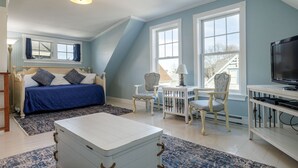 Ein Schlafzimmer mit einem Bett, zwei Stühlen, einem kleinen Tisch, einem Fernseher und einem großen Fenster.