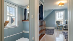 Ein Zimmer mit schrägem Dach, eingebauten Regalen, einem Sessel und einem Teppich.