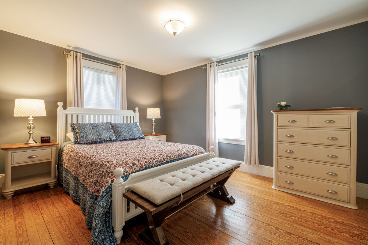 A bedroom with a bed, bench, nightstands, dresser, and lamps.