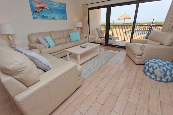 Relax in a comfortable living space with a sofa set, armchair, and coffee table, offering a view of the outdoor area with a pool and beach.