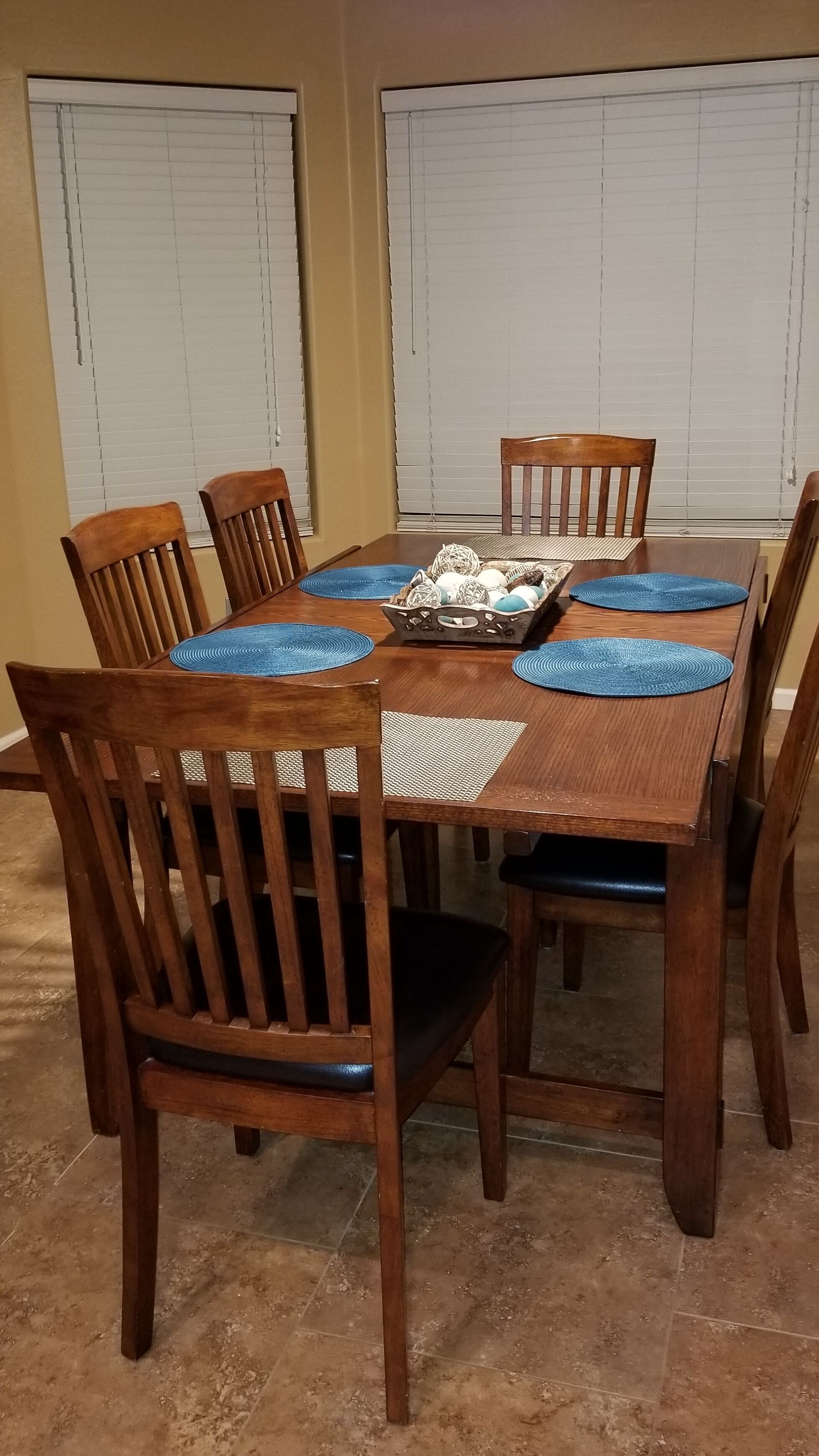 A dining table with six wooden chairs, blue placemats, and a decorative centerpiece.