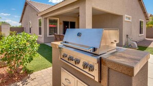 Une cuisine extérieure équipée d’un barbecue et d’un four, un espace patio et une maison en arrière-plan.