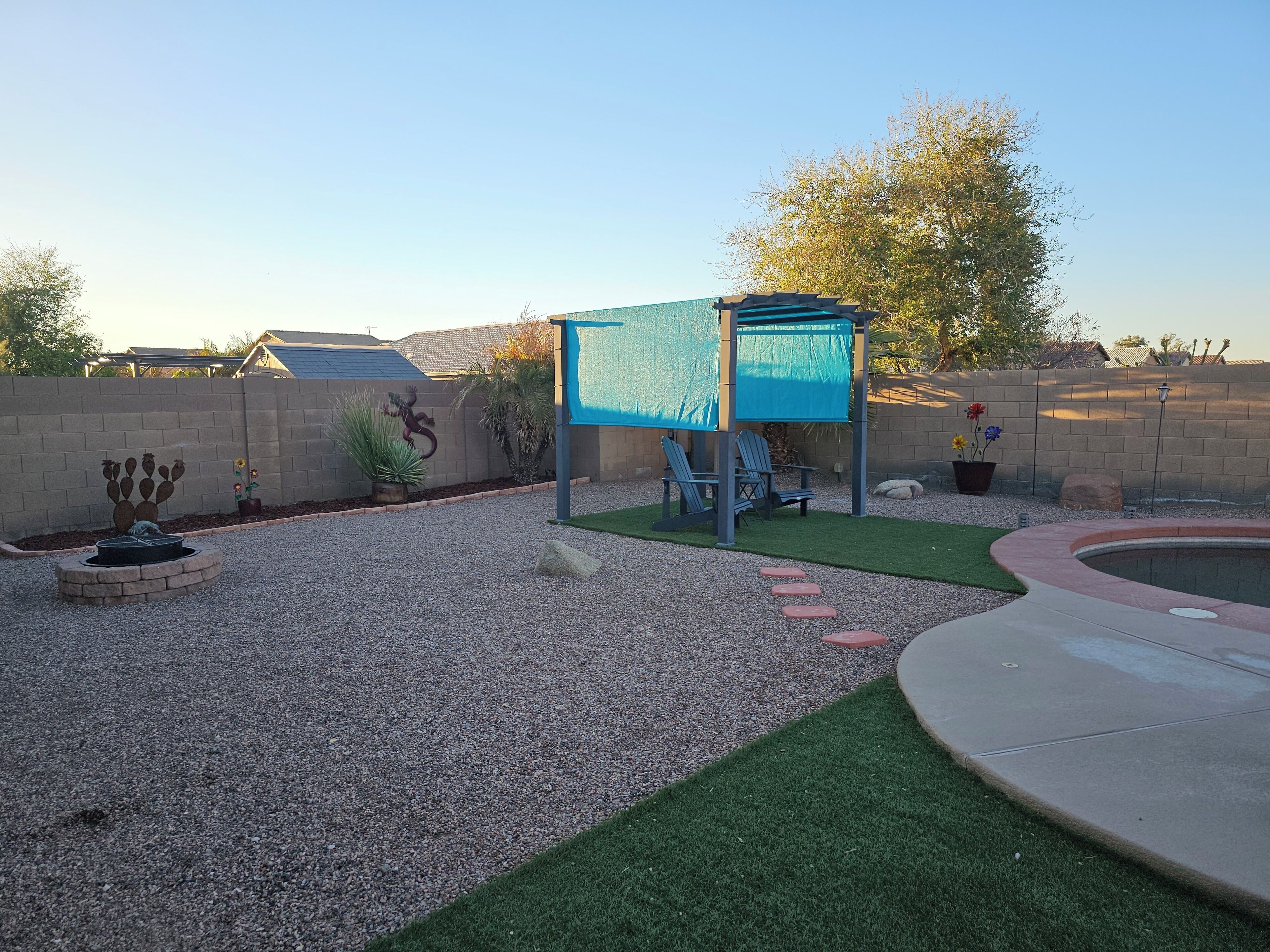 A backyard with a patio area, a small pool, and a cactus sculpture.