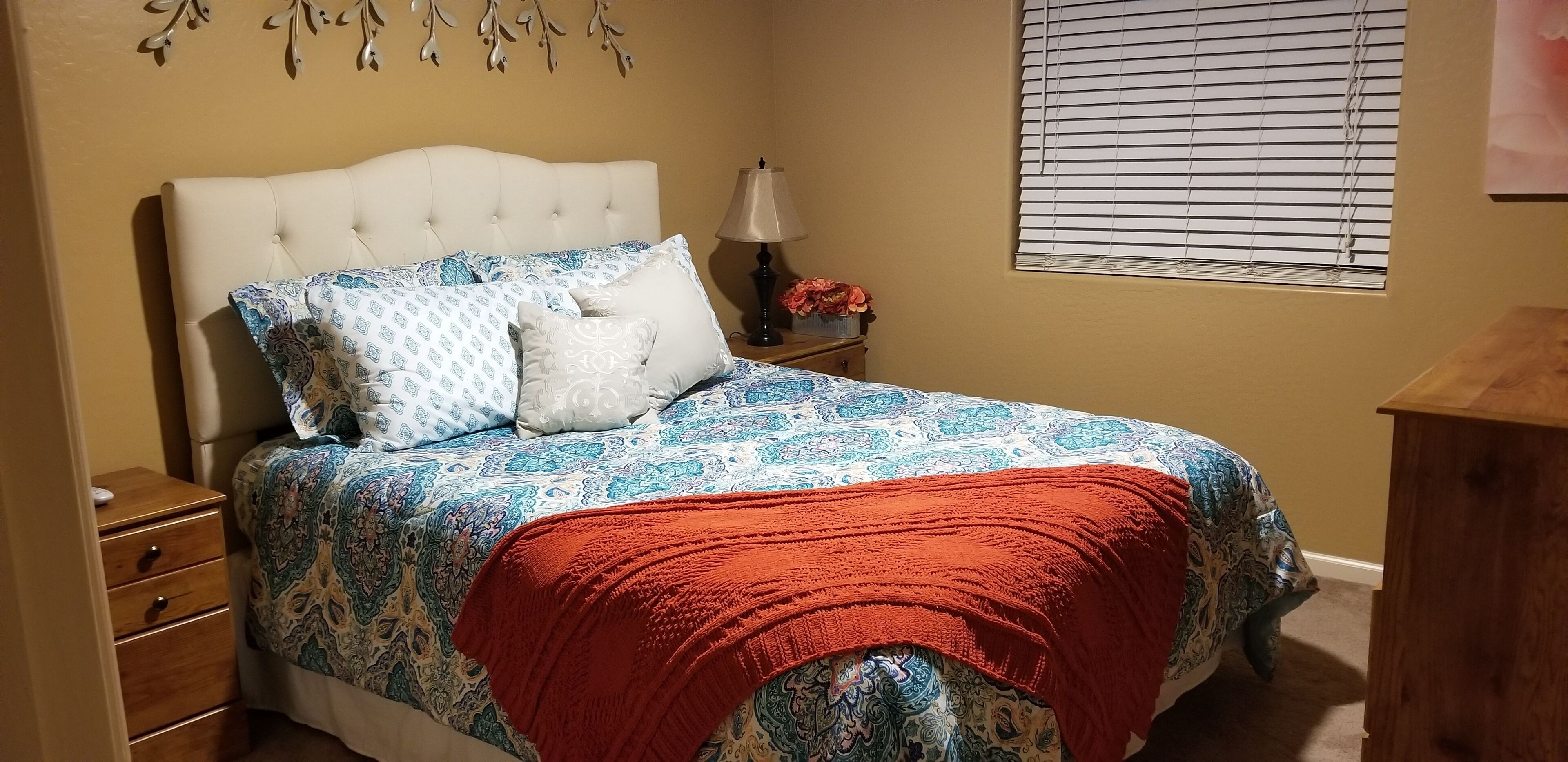 Een slaapkamer met een bed, nachtkastje, lamp en raam met zonwering.