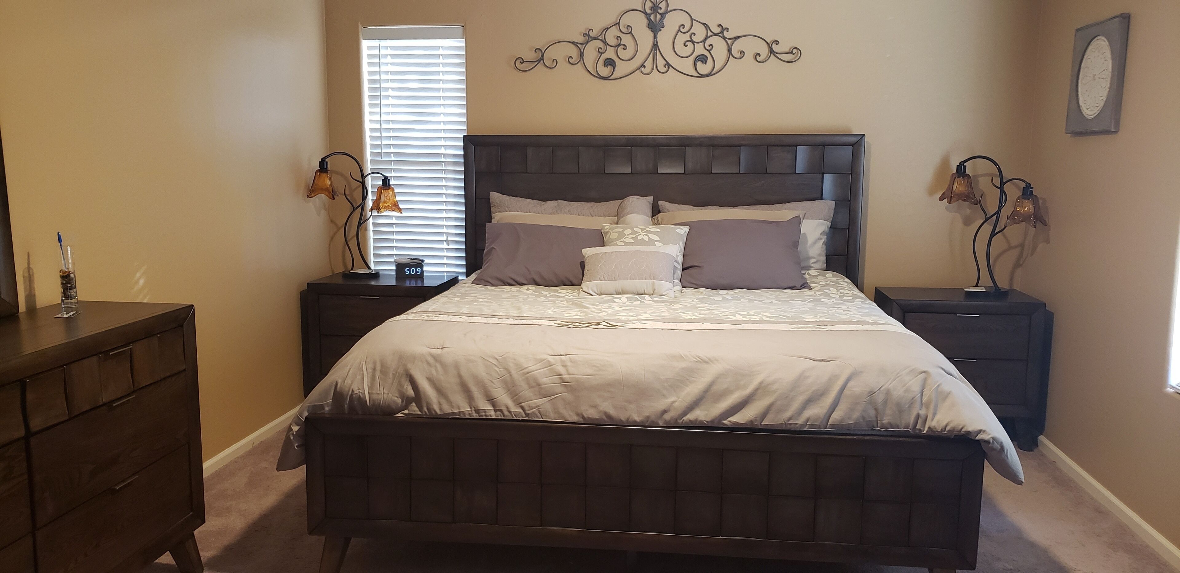 A bedroom with a large bed, two bedside tables, a dresser, and a wall clock.