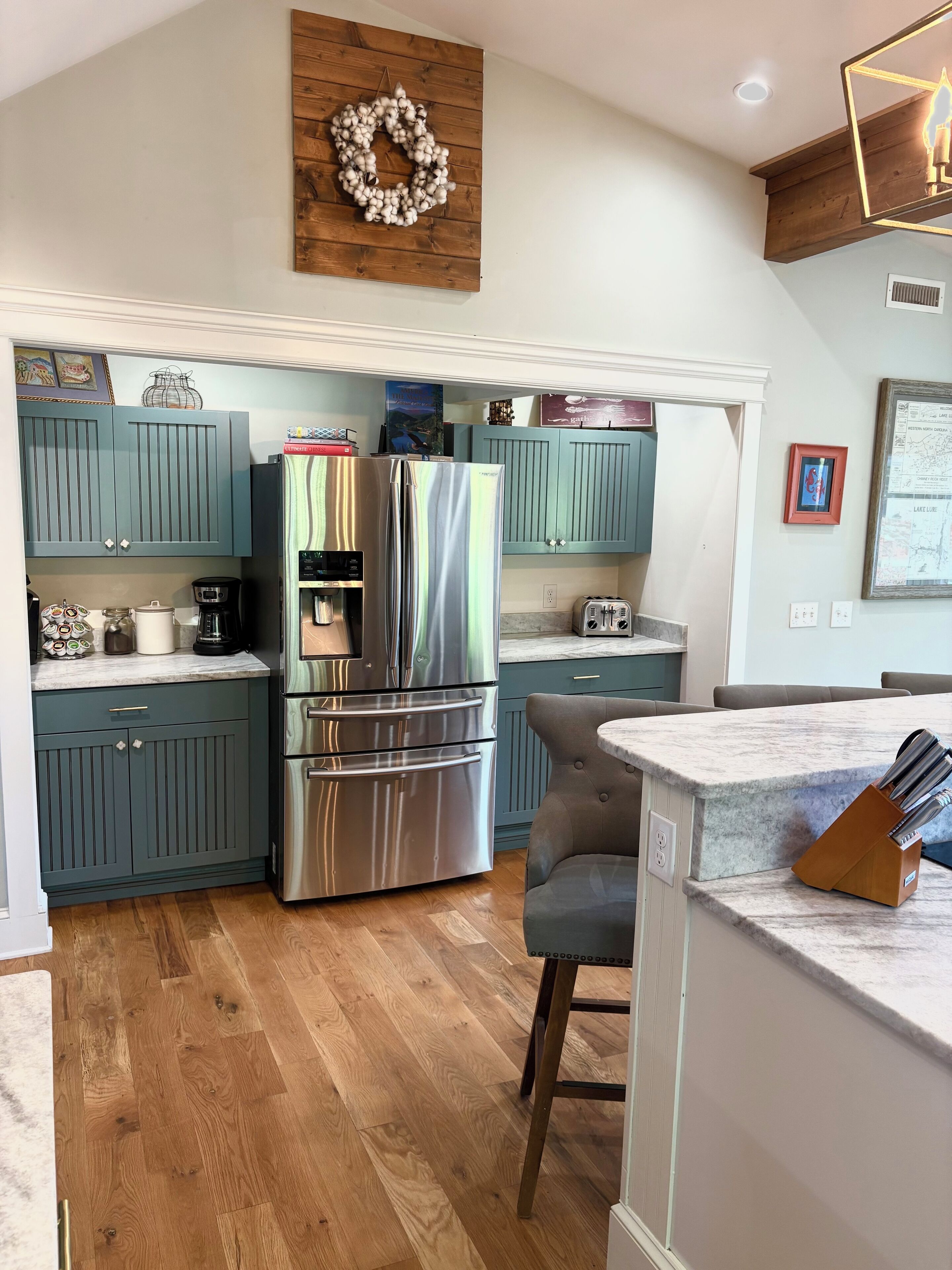 A modern kitchen with teal cabinetry, stainless steel appliances, and a wooden floor.
