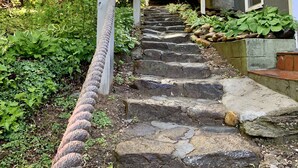 Una escala de pedra que puja cap a un edifici amb fonaments de pedra i un pont de fusta.