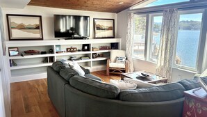 Un saló modern amb un sofà modular gran, un televisor fixat a la paret i vista a un llac a través de grans finestres.