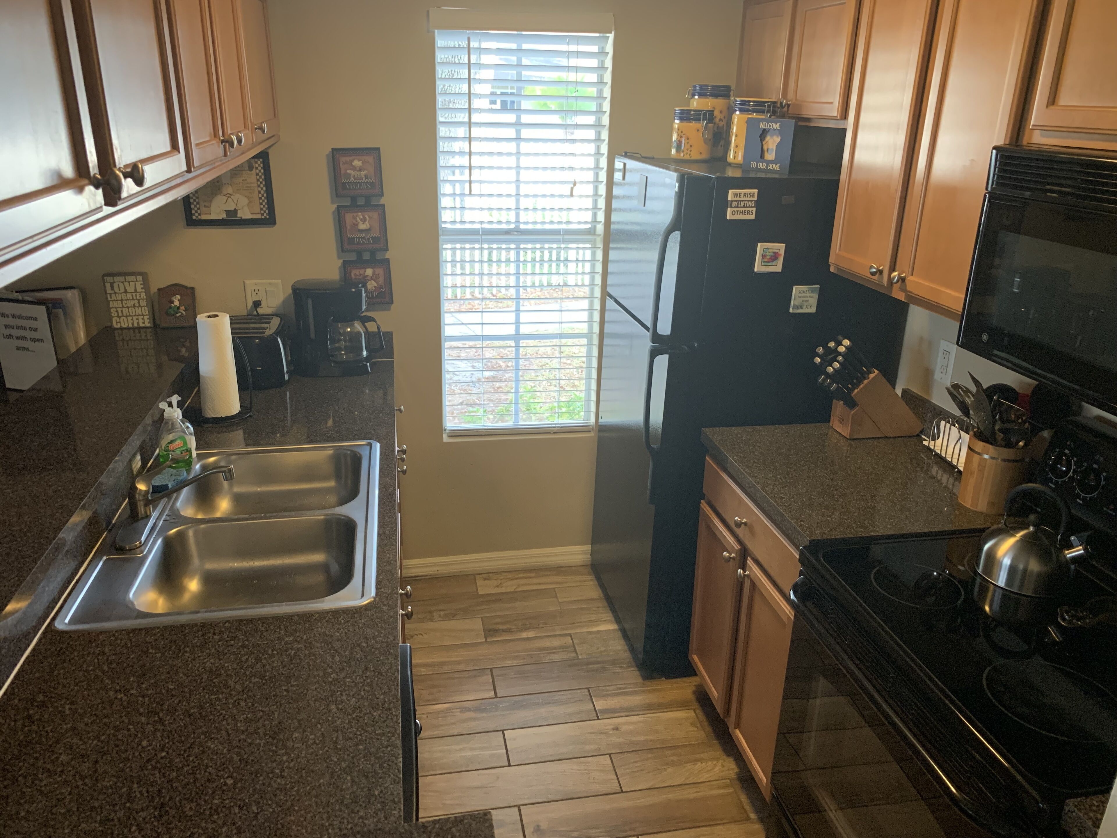 A kitchen with granite countertops, a stainless steel sink, a black refrigerator, a stove, and wooden cabinets.