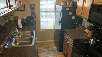 A kitchen with granite countertops, a stainless steel sink, a black refrigerator, a stove, and wooden cabinets.
