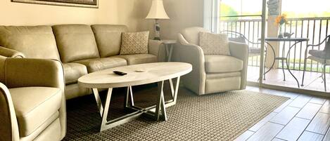 A living room with a sofa, armchairs, a coffee table, and a view of the outdoors through a sliding glass door.