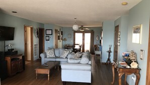 A living room with a sectional sofa, wooden flooring, a ceiling fan, and a television on the left. - Mother Ocean, Paradise, Oceanfront Panoramic Ocean Views, Private Beach (Holly Ridge)