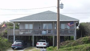 A two-story house with a covered porch, a flag, and two cars parked in front. - Mother Ocean, Paradise, Oceanfront Panoramic Ocean Views, Private Beach (Holly Ridge)
