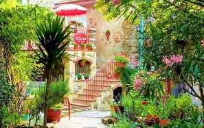A garden with a staircase leading to a building, surrounded by lush greenery and potted plants.