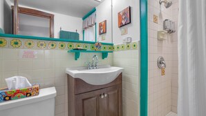 Un baño con un lavamanos blanco, un mueble de madera y una zona de ducha.