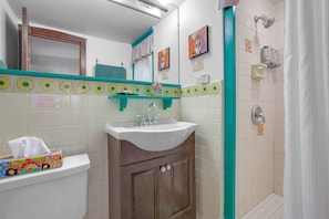 Bathroom features a sink, cabinet, mirror, and shower curtain, with a towel and shelf nearby.