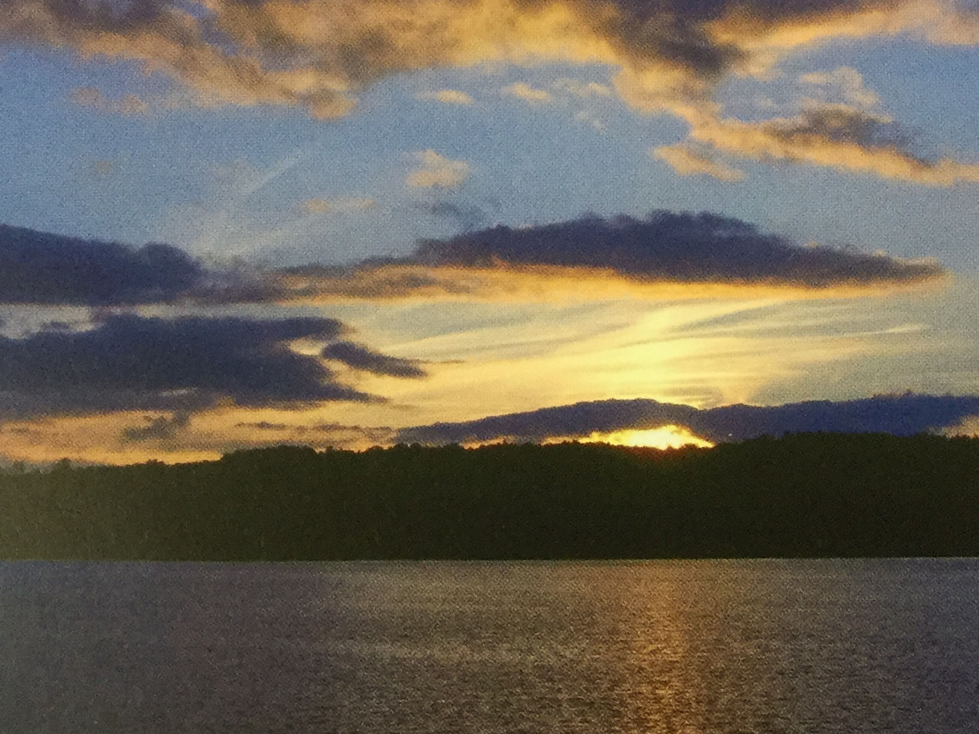 Auringonlasku vesistön yllä, jonka rannalla on metsää.