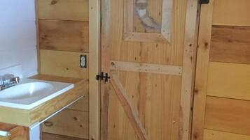 Une porte en bois avec un loquet métallique, un meuble en bois avec un évier et un sol carrelé.