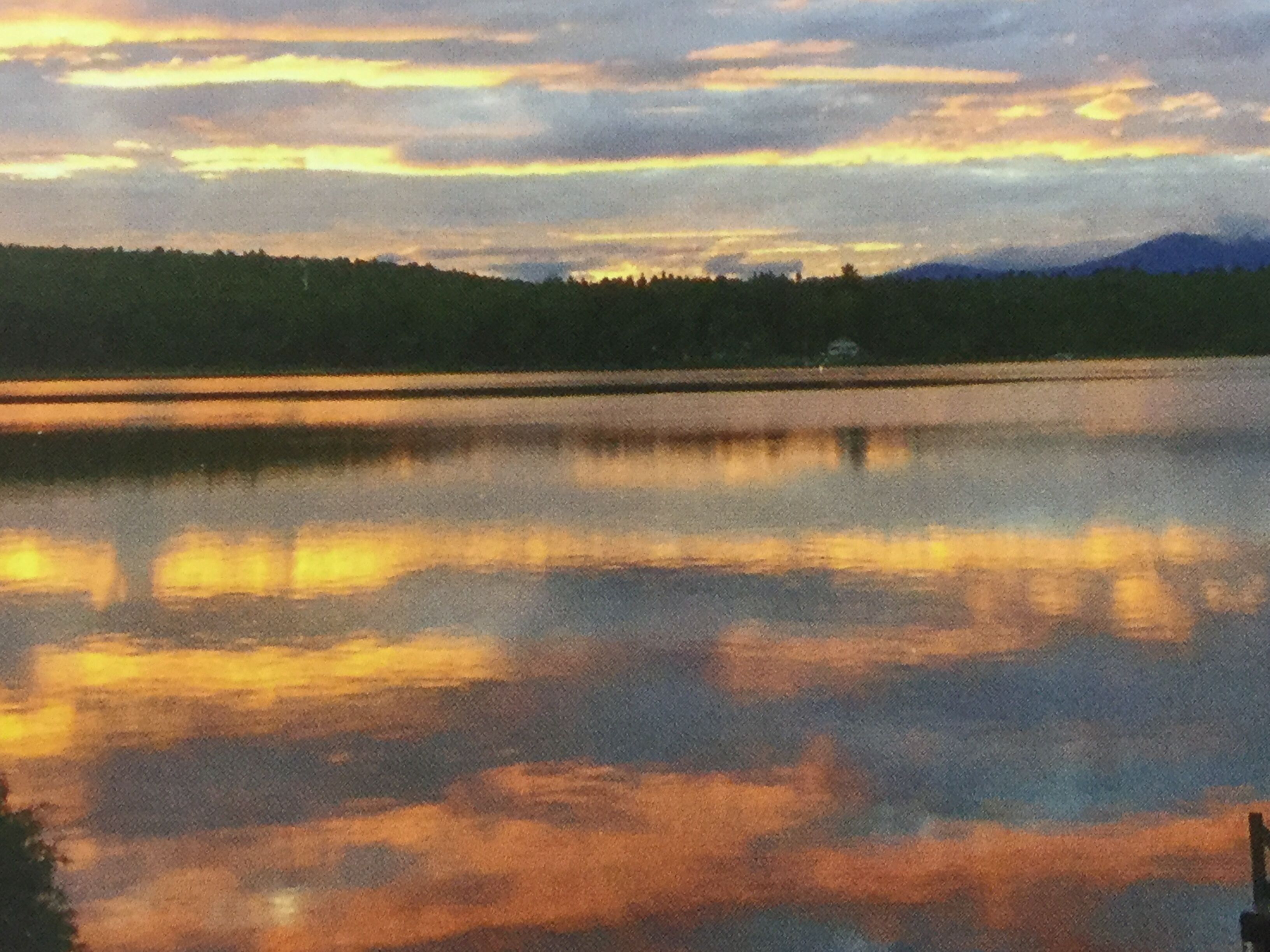 A calm lake with a forested shoreline and distant mountains.