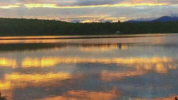 A calm lake with a forested shoreline and distant mountains.