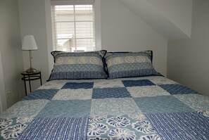 A bedroom with a bed, two pillows, a bedside lamp, and a window with blinds. - Carriage House - Best Kept Secret in Town (Rehoboth Beach)