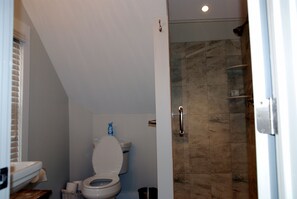 A bathroom with a toilet, a shower, and a tiled wall. - Carriage House - Best Kept Secret in Town (Rehoboth Beach)