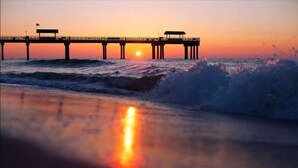 Ein Steg, der sich ins Meer erstreckt, mit untergehendem Sonnenuntergang im Hintergrund.