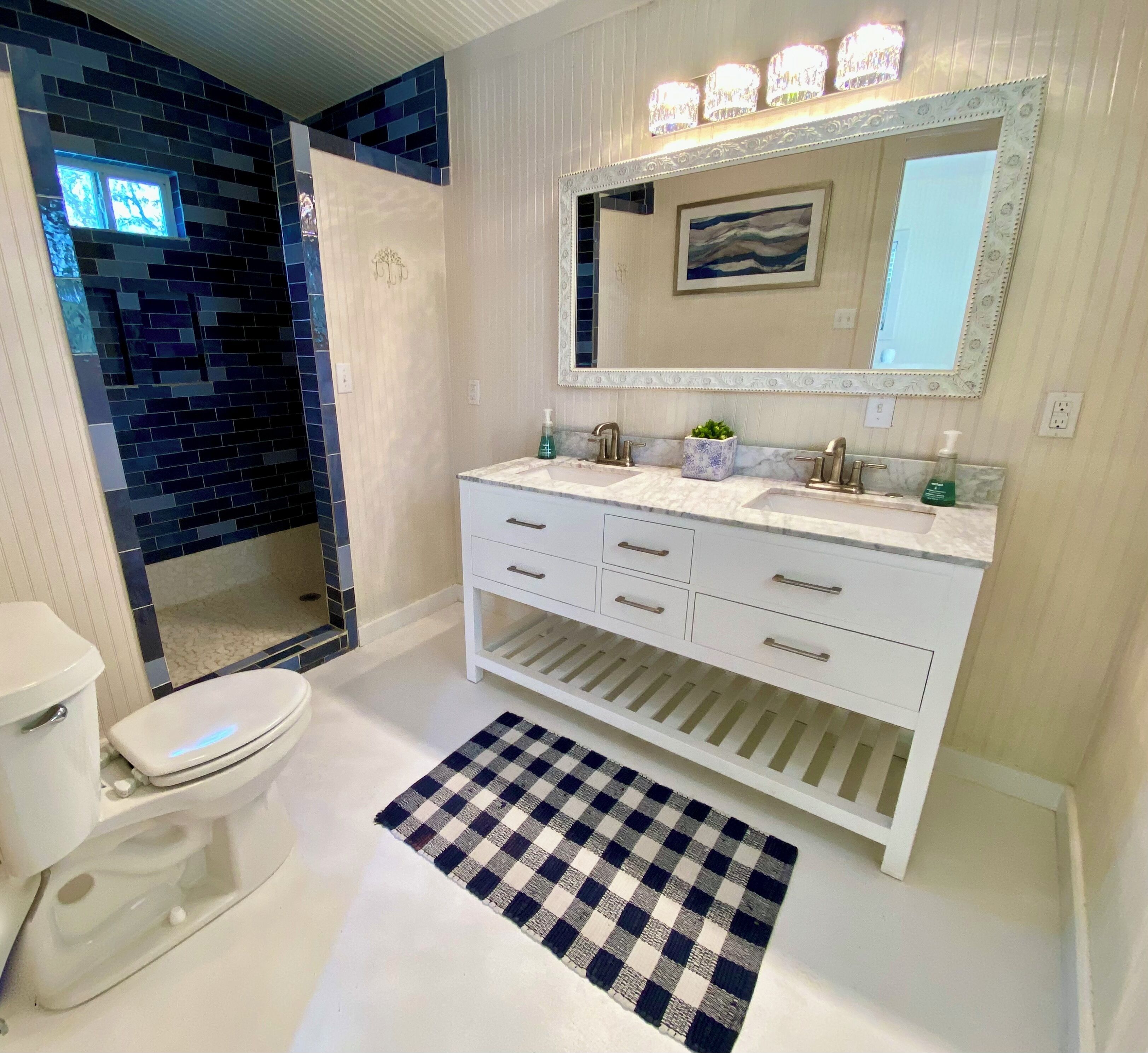 A bathroom with a white vanity, a large mirror, and a blue-tiled shower area.