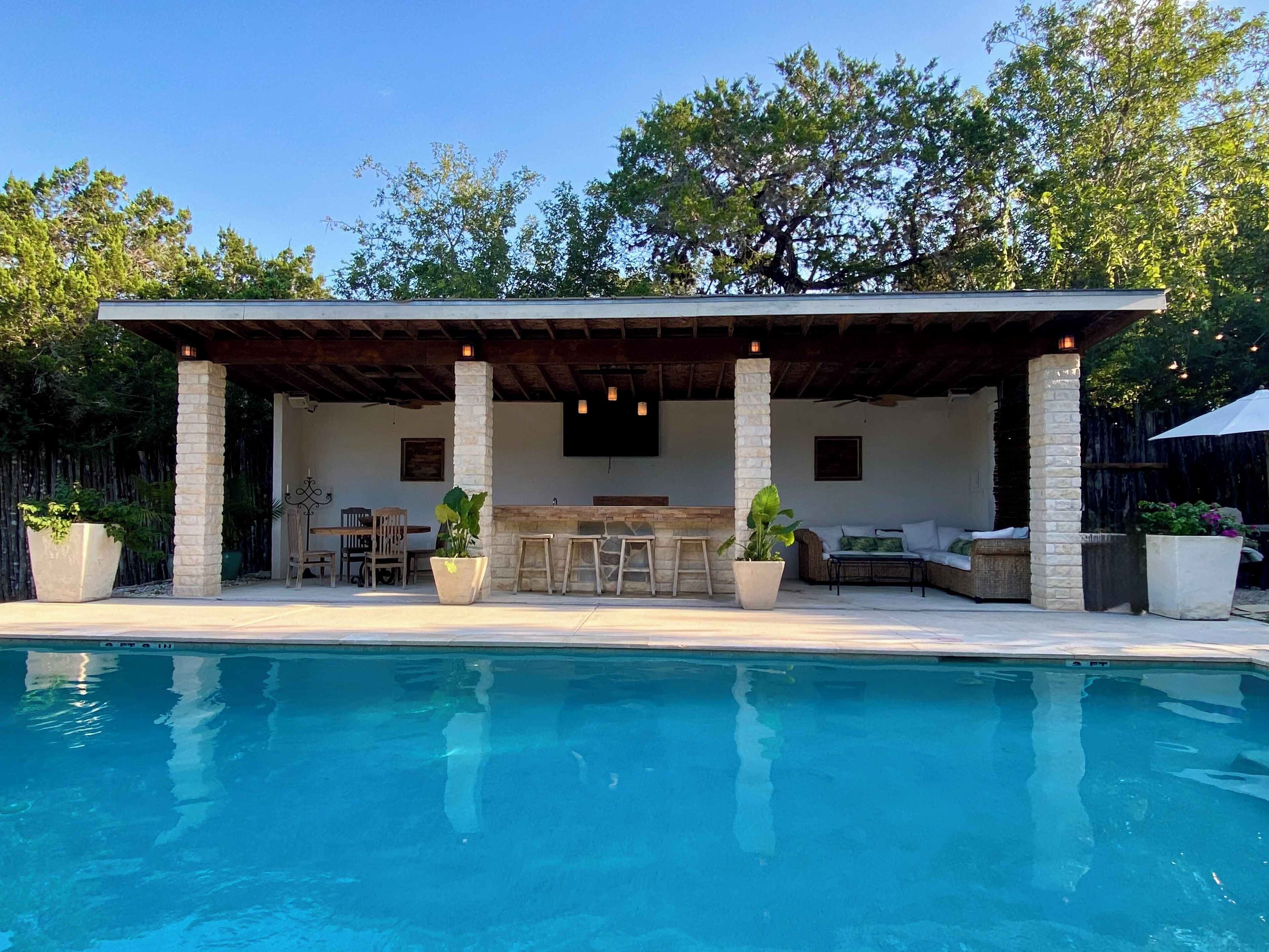 A poolside area with a covered seating area, stone pillars, and a bar.