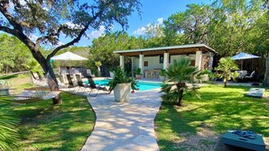 A backyard with a swimming pool, lounge chairs, and a covered patio area. - Historic Gated Estate, Pool, Cabana, 2 Kitchens, Lush, Kayaks, Walk 2 Frio! (Concan)