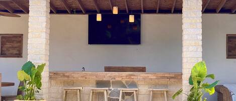 An outdoor bar area with stone pillars, wooden stools, and potted plants.