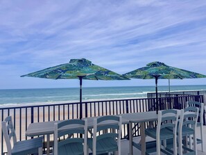 A seaside patio with two patterned umbrellas, a table, and chairs. - Newly Renovated Oceanfront Pool & Deck- GORGEOUS Ocean Views!!! (Daytona Beach Shores)