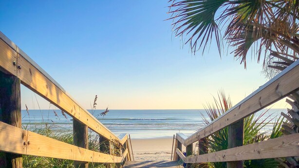 Un paseo marítimo de madera que conduce a una playa, con vista despejada al océano.
